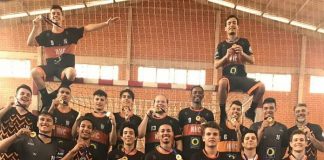 jogadores posam na quadra perfilados exibindo as medalhas e o troféu está no chão à frente da equipe