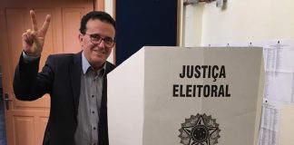 hélio faz sinal de vitória para a câmera ao lado da cabine de votação