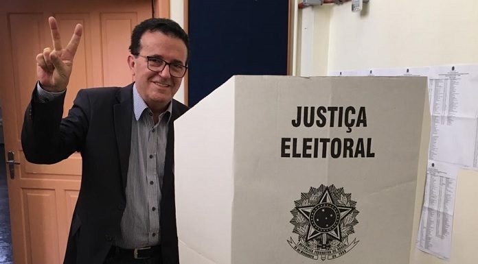 hélio faz sinal de vitória para a câmera ao lado da cabine de votação