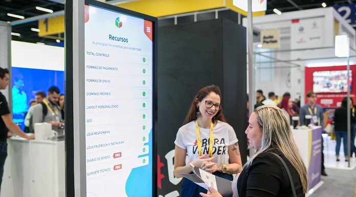 duas mulheres conversam entre si à frente de um grande tela em uma feira