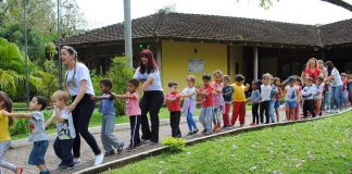 alunos e professoras fazem um trenzinho em área esterna com gramado da escola do meio ambiente