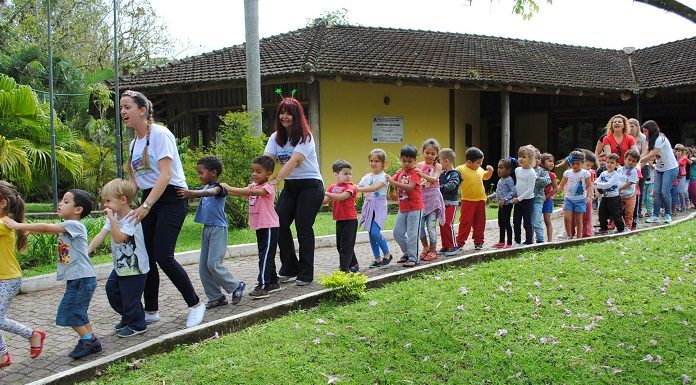 alunos e professoras fazem um trenzinho em área esterna com gramado da escola do meio ambiente