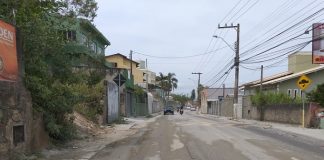 rua em que houve obra com parte de asfalto e outra de terra; carros ao fundo e casas ao lado