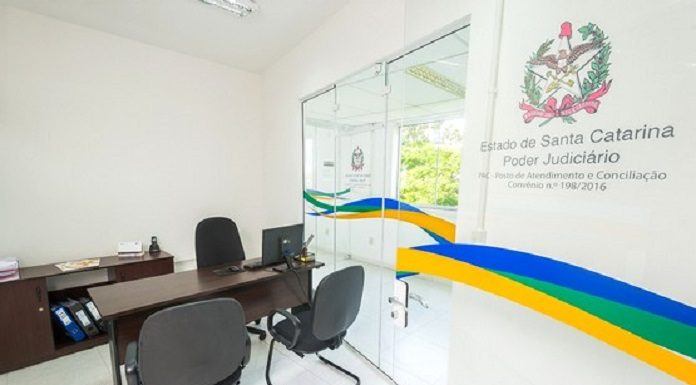 pequena sala de escritório com mesa e cadeiras e na parede o símbolo do tj