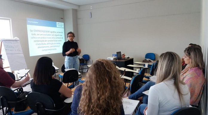 professora em pé fala a um pequeno grupo de alunos ao lado de uma projeção de texto na parede