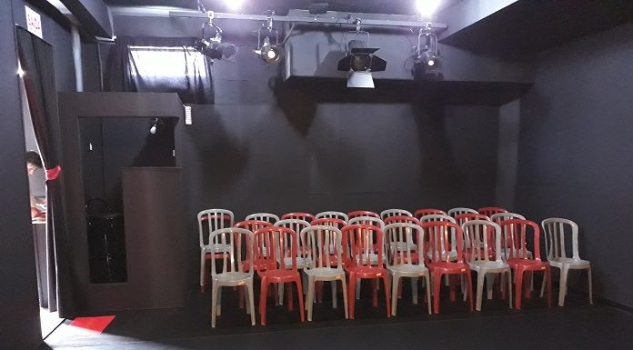 cadeiras de plásticos dispostas para plateia dentro de uma sala totalmente preta para o teatro