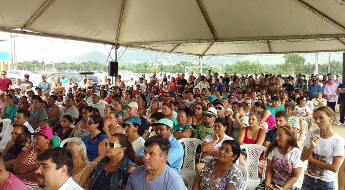 grande grupo de pessoas sentadas em plateia sob tenda olha na mesma direção