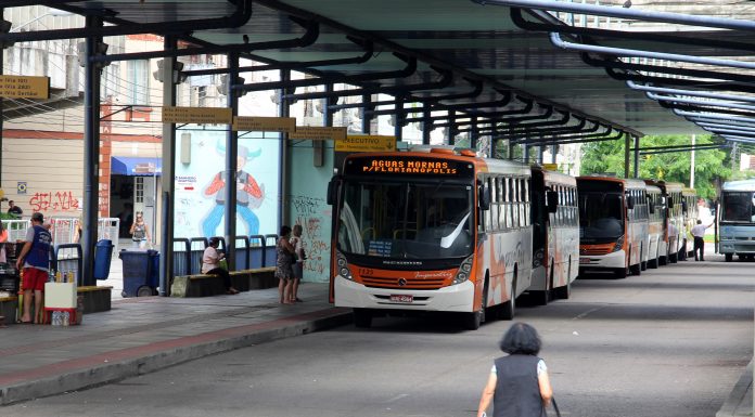 mulher caminha em direção a plataforma do terminal, onde há dois ônibus estacionados