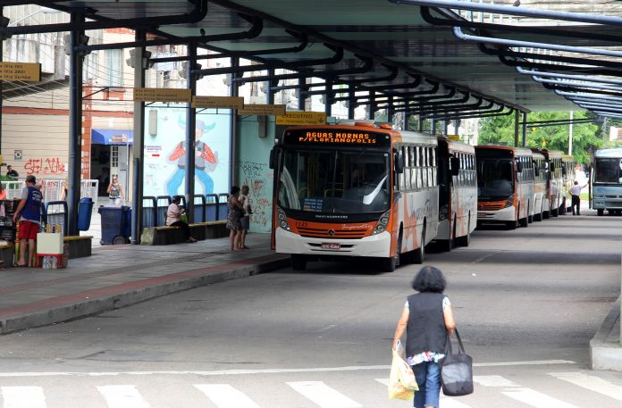 mulher caminha em direção a plataforma do terminal, onde há dois ônibus estacionados