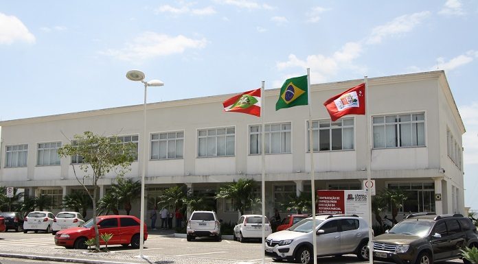 fachada do prédio da camara com alguns carros estacionados à frente e bandeiras hasteadas