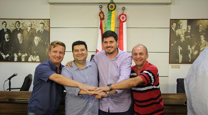 os quatro vereadores de mãos dadas posam para a foto em frente à mesa diretora da cmsj