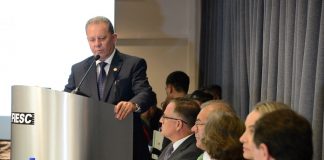 ponticelli falando na tribuna da fiesc ao lado de uma bancada com outros políticos