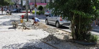 pedras do calçadão do kobrasol empilhadas em pequenos montes e trabalhador agachado arrumando em dia de sol