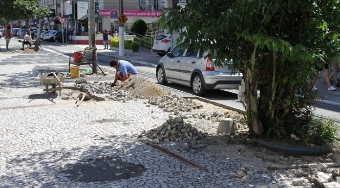 pedras do calçadão do kobrasol empilhadas em pequenos montes e trabalhador agachado arrumando em dia de sol