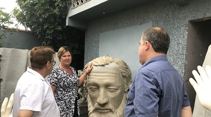 prefeita adeliana apoiada na cabeça da estátua, que é quase do seu tamanho, conversando com dois homens