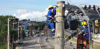 dois operários com equipamentos de proteção trabalham em ligação da rede elétrica no alto de um poste