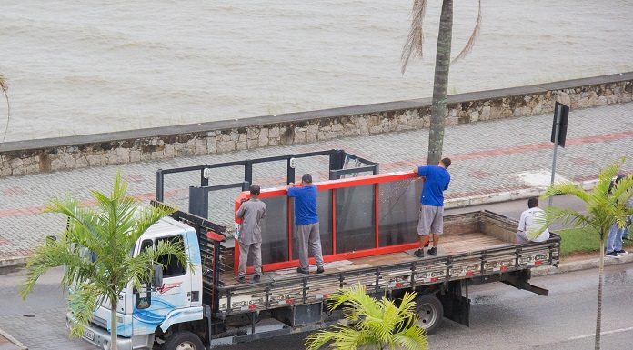 trabalhadores em cima de um caminhão colocam placa sobre um ponto de ônibus em uma avenida com coqueiros