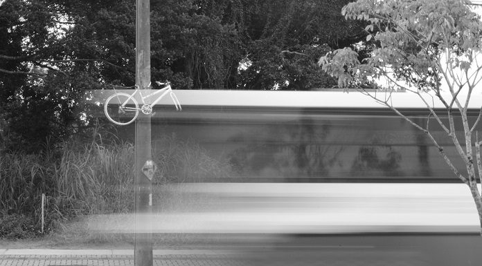 imagem em preto e branco e borrada de um ônibus passando em velocidade em frente a uma bicicleta fantasma