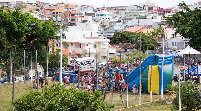 foto de praça com muita gente, brinquedos, arvores, e casas ao fundo