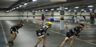 três patinadoras disputam corrida em um estacionamento coberto