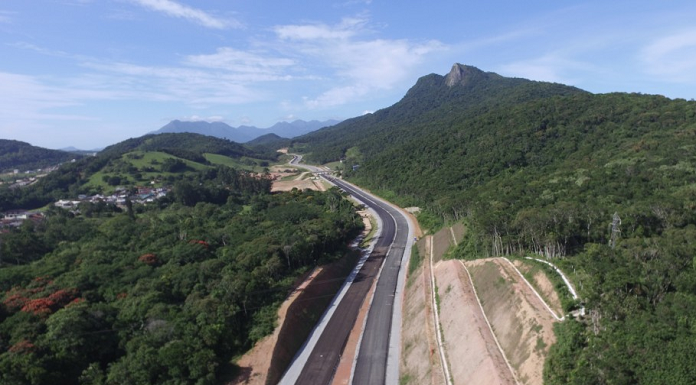 obra do contorno viário vista do céu: duas pistas novas sem pintura cortando região de mata e morros