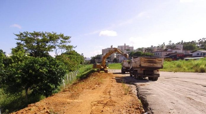 retroescavadeira coloca terra em caminhão parado sobre terraplanagem