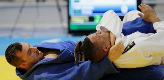 homem de quimono azul dá golpe de enforcamento no chão em outro homem de quimono branco