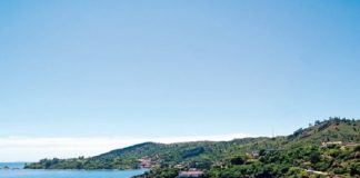 vista superior da praia calma com alguns barcos na água e morros com muita vegetação em volta