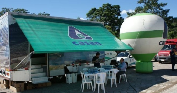 trailer da casan estacionado com toldo aberto com logo da companhia, balão inflável e mesas com cadeiras à frente