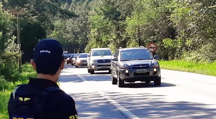 policial no ascostamento de rodovia no meio da mata observa carros passando