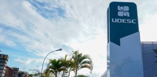 torre com inscrição da udesc no topo ao lado de prédio e estacionamento do campus