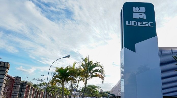 torre com inscrição da udesc no topo ao lado de prédio e estacionamento do campus