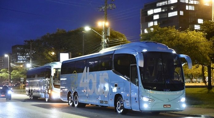 dois ônibus passando por rua arborizada caracterizados com o logo 4bus