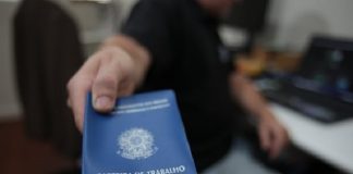 homem aponta para a câmera uma carteira de trabalho e previdência social