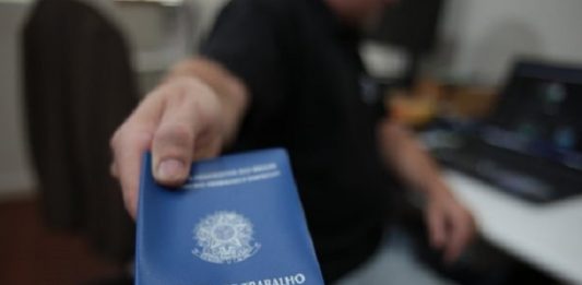 homem aponta para a câmera uma carteira de trabalho e previdência social