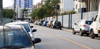 carros estacionados nos dois lados de uma rua asfaltada com prédios em volta