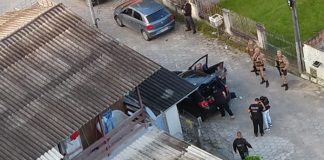 foto aérea de casa com telhado de zinco com diversos policiais na frente da casa na rua