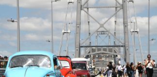 fuscas e outros carros antigos passando sobre a ponte Hercílio Luz com pessoas em volta