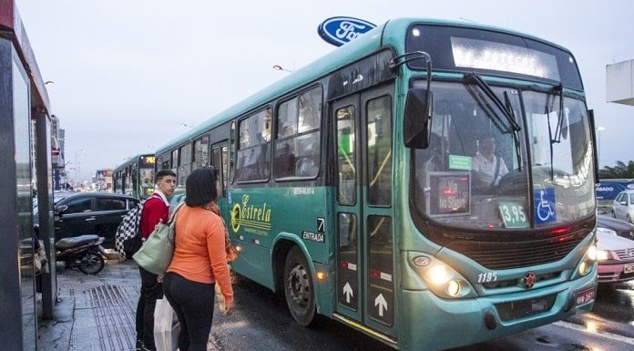 ônibus da empresa estrela parado ao lado de ponto onde há um homem e uma mulher em pé em um dia chuvoso