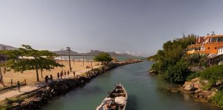 barco de pesca artesanal passando pelo canal da barra da lagoa em dia de água tranquila e sol, visto de cima