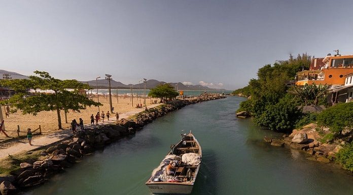 barco de pesca artesanal passando pelo canal da barra da lagoa em dia de água tranquila e sol, visto de cima