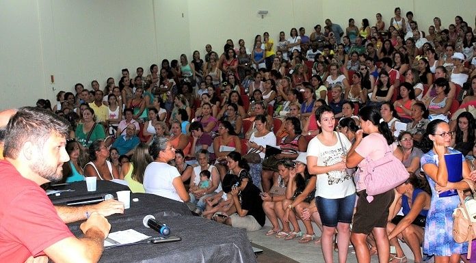 auditório lotado, a maioria mulheres, com algumas pessoas sentadas em palco à frente em uma mesa