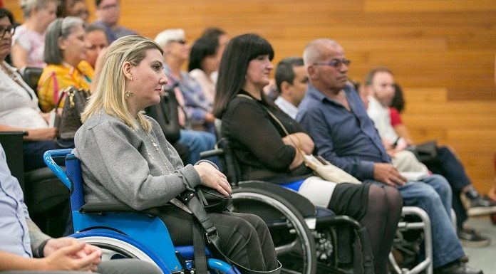 mulheres e homens em cadeiras de roda à frente das poltronas de um auditório com outras pessoas sentadas