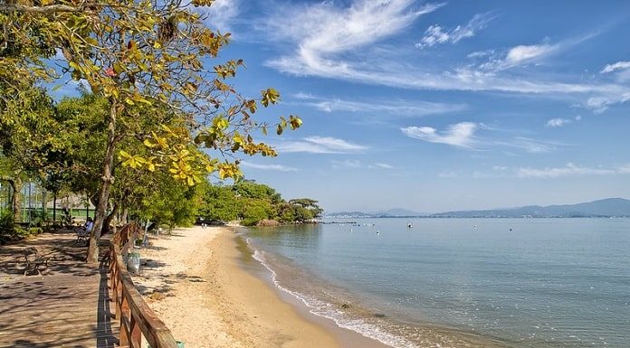 praia de sambaqui com mar parado em dia de sol, praia vazia e deck na orla