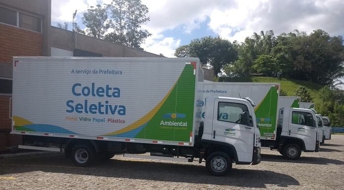 quatro caminhões de coleta de lixo seletiva com logo da ambiental estacionados lado a lado de ré para um edifício