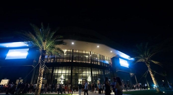 fachada iluminada da arena petry com dezenas de pessoas na frente em foto noturna