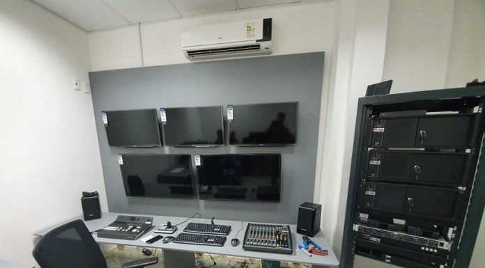 pequena sala com aparelhagem eletrônica: cinco monitores na parede e teclados em uma mesa