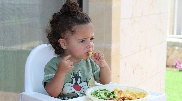 menina comendo em cadeirote infantil com prato de legumes a sua frente