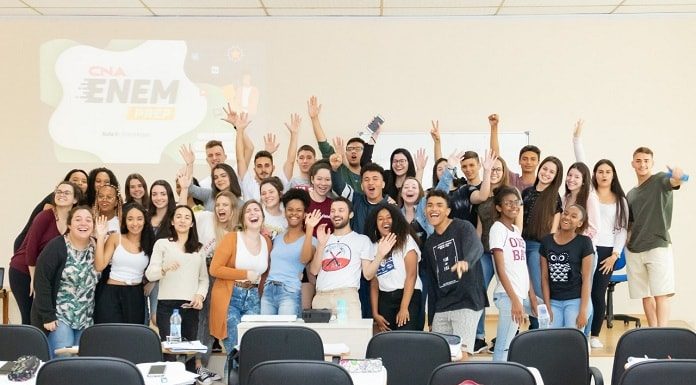 alunos e alunas em pé na frente da sala posam animados para a foto