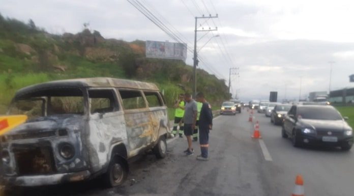 kombi totalmente destruída pelo fogo com homens e cones em volta, carros passando ao lado